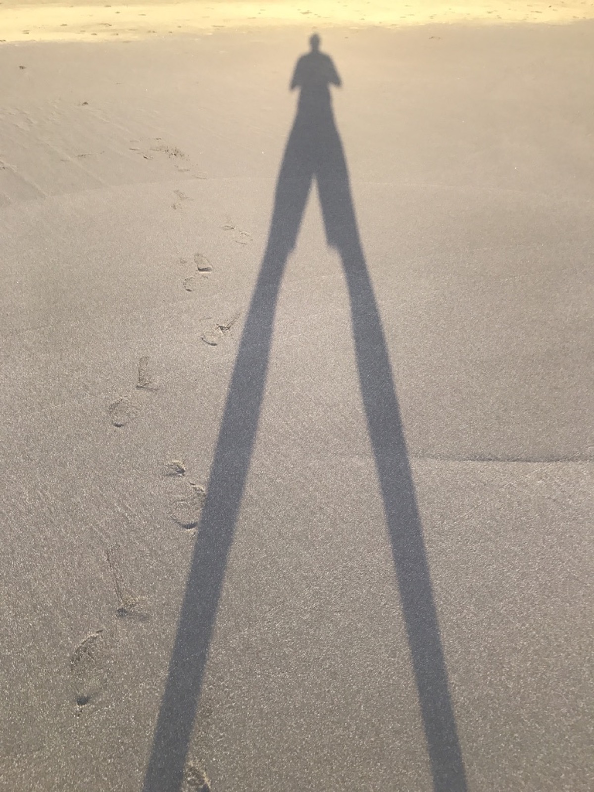A long shadow cast across rippled beach sand