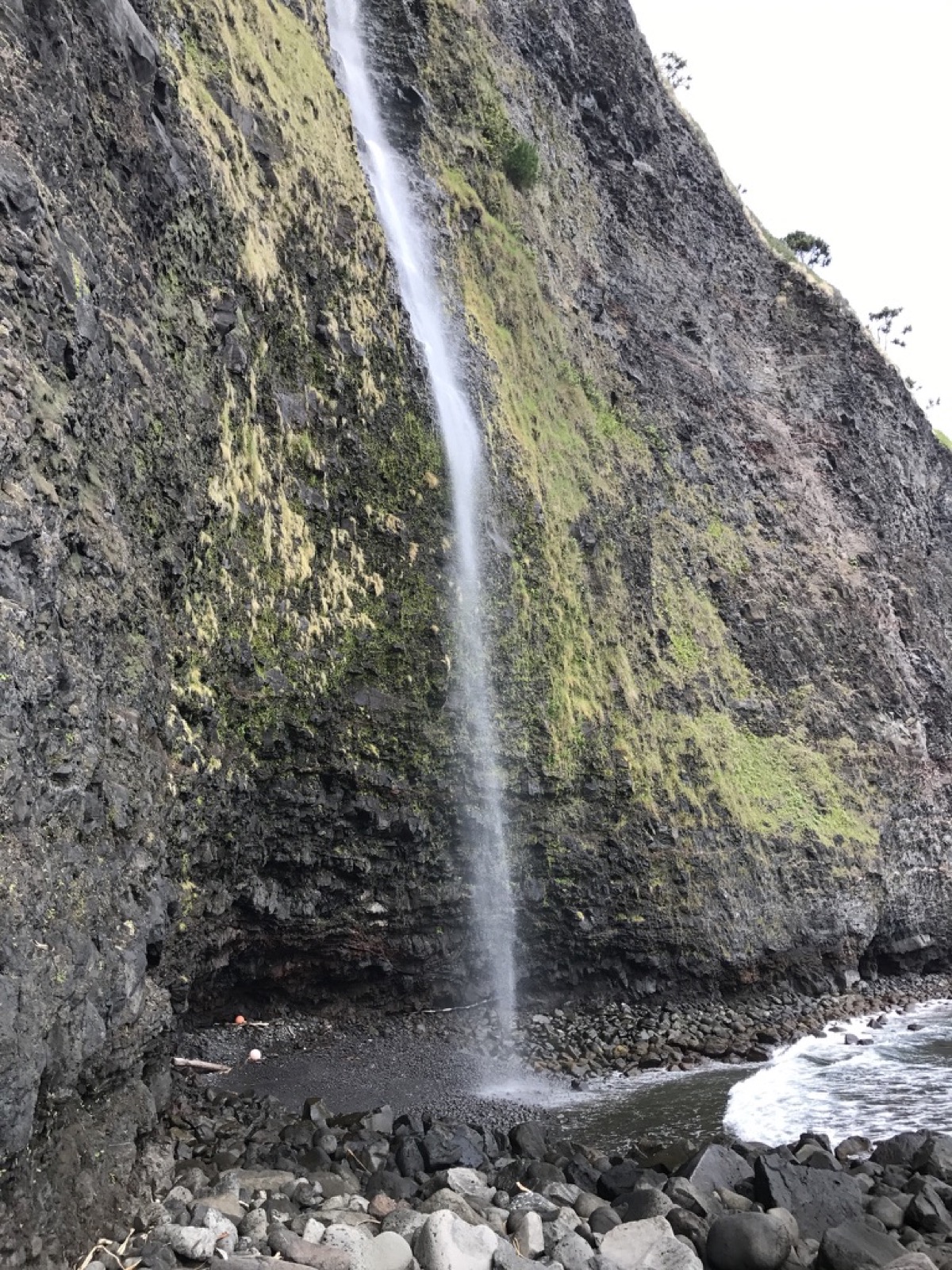 A tall waterfall falling to a boulder beach